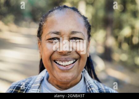 Ältere afrikanerin lächelt vor der Kamera mit Wald im Hintergrund - Fokus auf Gesicht Stockfoto