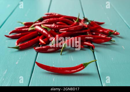 Rote Paprikaschote vor rohen Chilischoten stapeln sich auf einem türkisfarbenen Holztisch. Ganze frische scharfe Chilies zum Kochen würziger Gerichte. Stockfoto