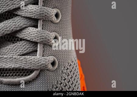 Sneakers aus grauem Mesh-Material mit Schnürung, Makroaufnahme. Spitzenverschluss der neuen orangenen Sportschuhsohle aus nächster Nähe. Moderne Textilschuhe elastische Schnürsenkel. Speicherplatz kopieren. Stockfoto