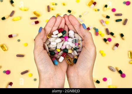 Viele bunte Pillen in den Händen einer Frau vor dem Hintergrund von verstreuten Kapseln. Zusatz- und Gesundheitsprodukte, Draufsicht. Stockfoto