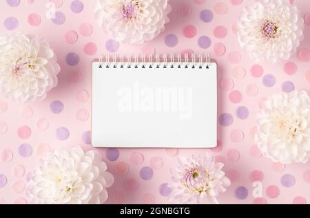 Komposition aus geöffnetem Notizblock, eingerahmt von weißen Blumen und farbenfrohen runden Konfetti auf trendigem rosafarbenem Hintergrund. Schöne flache Lay mit Kopieplatz für Ihr Design. Urlaubskonzept. Stockfoto