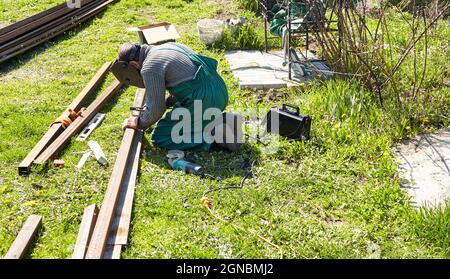 Schweißarbeiten. Ein Mann Schweißer mit Bauhandschuhen und einer Schweißmaske, die mit einem Metall im Freien arbeitet Stockfoto