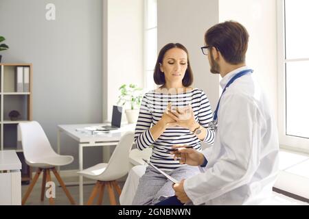 Eine besorgte Patientin mittleren Alters erklärt ihrem Arzt die Symptome und klagt über Herzschmerzen. Stockfoto