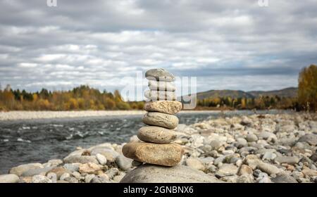 Steinhaufen, der in einem Kairn auf dem Hintergrund des Flusses gebaut wurde. Konzept von Ruhe und Loslösung mit der Natur Stockfoto