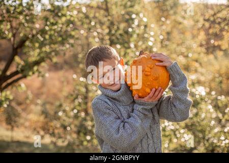 Deformierte hässliche orangefarbene Kürbisse in den Händen eines Kindes. Stockfoto