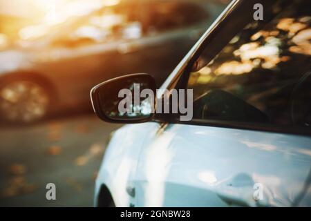 Ein verschwommenes Bild des Rückspiegels auf einem weißen Auto und eine schöne Spiegelung auf seinem Seitenfenster an einem sonnigen Herbsttag. Verkehr. Stockfoto