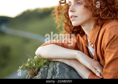 Cropped Tourist liegt auf Wiese in Bergfelsen am Abend, Straße im Hintergrund, entspannen nach der Wanderung, Klettern, Weibchen schaut auf Seite in c Stockfoto