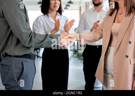 Beschnitten zwei kaukasische Geschäftsleute schüttelten sich im modernen Büro mit Kollegen die Hände. Mann und Frau in formeller Kleidung. Konzept der Partnerschaft und Kommunikation Stockfoto