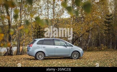 Das Auto befindet sich in einem ruhigen Herbstwald. Goldene Bäume, der Boden ist mit leuchtend gelben Blättern bedeckt. Reisekonzept, schöne Natur und Herbststimmung Stockfoto
