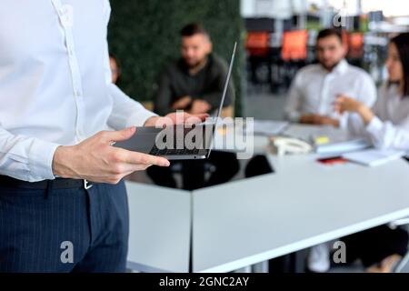 Das Business-Team sitzt in einem modernen, hellen Büro, während sich der Geschäftsmann auf die Rede vorbereitet, den Laptop in den Händen hält und einen kurzgeschnittenen Mann in klassischer formeller Kleidung trägt Stockfoto