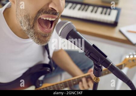 Nahaufnahme des Gesichts eines nicht erkennbaren emotionalen männlichen Sängers, der im Studio ins Mikrofon singt. Stockfoto