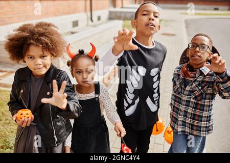 Eine Gruppe afroamerikanischer Kinder, die Halloween-Kostüme tragen und für die Kamera posieren, während sie zusammen tricksen oder sich behandeln Stockfoto