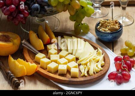 Eine Vorspeise mit verschiedenen Käsesorten, Trauben und Walnüssen, serviert mit Wein. Rustikaler Stil. Stockfoto