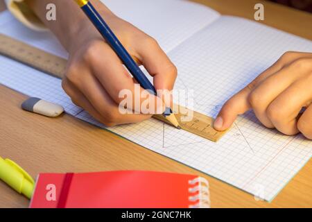 Ein Student zeichnet mit einem Bleistift eine Linie in einem Notizbuch entlang eines Lineals. Ein Schuljunge erledigt eine Aufgabe am Arbeitsplatz. Das Konzept der Kindererziehung, Vermittlung von Wissen, Fähigkeiten und Fähigkeiten. Stockfoto