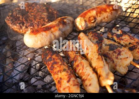 Fleisch wird auf einem unverschämmbaren Grill am Strand gekocht. England, Großbritannien. Burger, Würstchen, Kebabs. Stockfoto