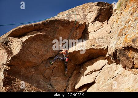 Die junge Sportlerin klettert bei Sonnenuntergang in der Nähe des Flusses Ili in Kasachstan auf den hohen Felsen Stockfoto