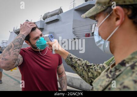 SAN DIEGO (29. Mai 2020), Ein Seemann, der dem Lenkraketen-Zerstörer USS Kidd (DDG 100) zugewiesen wurde, lässt seine Temperatur überprüfen, als er als Teil der aggressiven Reaktion der Marine auf den COVID-19-Ausbruch zum Schiff zurückkehrt. Um für die Rückkehr zum Schiff freigegeben zu werden, müssen die Segler zwei separate negative Testergebnisse erhalten haben. Kidd kam am 28. April in San Diego an, um medizinische Versorgung für seine Seeleute zu erhalten und das Schiff nach einem COVID-19-Ausbruch zu reinigen und zu desinfizieren. Die Besatzung wird die strategische Tiefenreinigung gemäß den etablierten Marine- und Centers for Disease Co. Fortsetzen Stockfoto