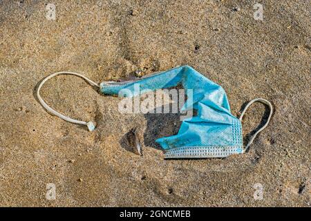 Weggeworfene Einweg-Gesichtsmaske / Gesichtsmaske an Land gewaschen, verschmutzt Sandstrand entlang der Küste während COVID-19 / Coronavirus / Corona-Virus Pandemie Stockfoto