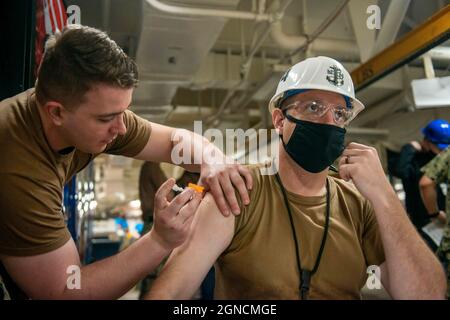 NORFOLK (25. Mai 2021) Chief Aviation Support Equipment Technician Andrew Couillard, rechts, aus Iron Mountain, Michigan, der dem Flugzeugträger USS John C. Stennis (CVN 74) zugewiesen wurde, erhält den COVID-19-Impfstoff vom Hospitalman Henry Mason aus Uhrichsville, Ohio, der dem Flugzeugträger USS George Washington (CVN 73) zugewiesen wurde, In the Mess Decks an Bord von John C. Stennis in Newport News, Virginia, 25. Mai 2021. Die John C. Stennis befindet sich in der Newport News Werft für eine komplexe Betankung als Teil der Mission, das Kriegsschiff im Kampf wieder rechtzeitig und im Rahmen des Budgets zu liefern, um wieder aufzunehmen Stockfoto