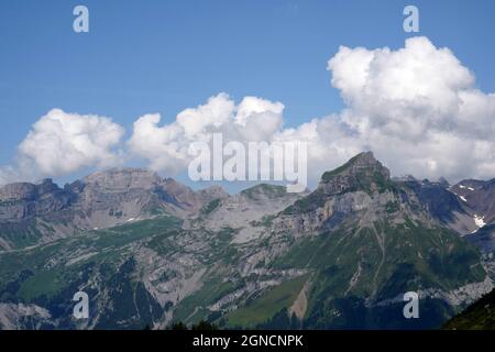 Berge rund um das Dorf Engelberg in der Schweiz im Sommer. Alpwiesen in den Bergen sind dunkelgrün. Es kommen dicke weiße Wolken Stockfoto