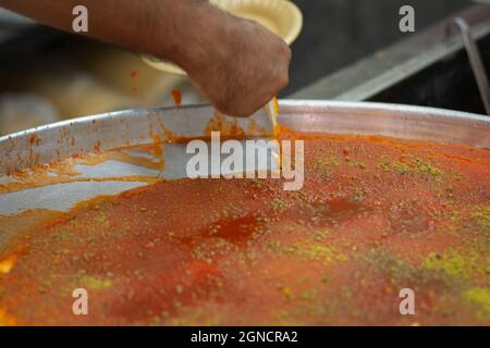 Man schneidet von Hand ein Stück Kanafeh, ein traditionelles köstliches Dessert aus dem Nahen Osten, serviert auf einem weißen Teller Stockfoto