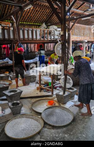 Die Atmosphäre, in der Reismehl in einer traditionellen Kuchenfabrik hergestellt wird, Frauen, die Reis mit einem Steinmörtel und Stößel aus Holz zu Mehl mahlen. Stockfoto
