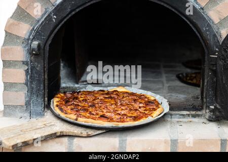 Pizza aus einem weiß lackierten, handgefertigten Holzofen, der auf der Außenseite gebaut wurde Stockfoto
