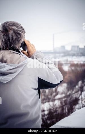 Ein älterer Mann, der am Telefon telefoniert und die Pflanze aus der Nähe betrachtet. Stockfoto