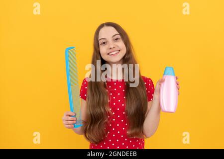 Happy Kid lange Haare zeigen Conditioner und Kamm auf gelbem Hintergrund, Haarpflege Stockfoto