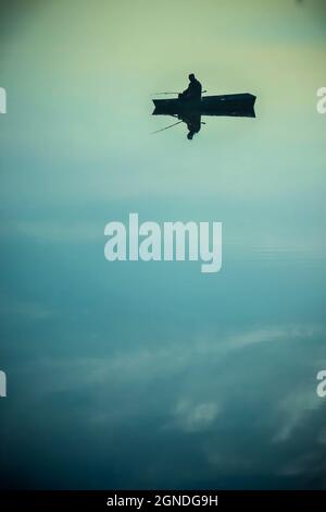 Schwarze Silhouette des Mannes in einem kleinen Boot auf dem See Stockfoto