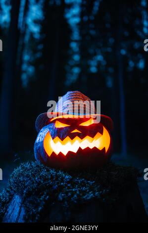 Ein gruseliger Kürbis mit einem geschnitzten Gesicht in einem düsteren Wald an Halloween. Stockfoto