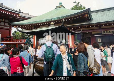 Menschenmenge versammelt sich um einen Weihrauchbrenner im Sensoji-Tempel, der Rauch bedeckt oder mit Rauch badet, bevor im Gebetsraum gebetet wird. Stockfoto