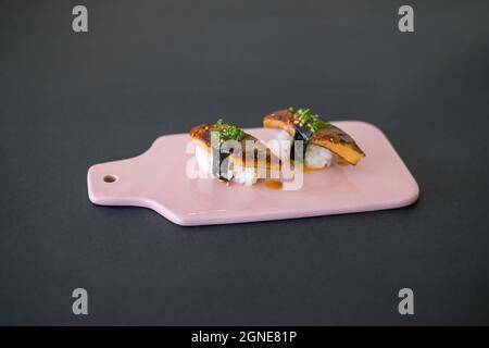 Japanisches Sushi - zwei Unagi Nigiri Sushi auf hellrosa Tafel. Sushi-Stücke werden auf Schiefer serviert, der auf schwarzem Hintergrund isoliert ist. Sushi mit hinterem Aal Stockfoto