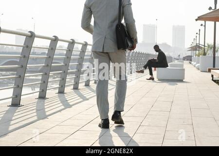 Horizontale Rückansicht eines unverkennbaren Mannes in Anzug, der irgendwo in der modernen Stadt auf der Straße spazieren ging Stockfoto