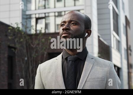 Horizontales, mittleres Nahaufnahme-Porträt eines hübschen afroamerikanischen Mannes mit Bart im Gesicht, der Ohrstöpsel trägt und draußen Musik hört Stockfoto