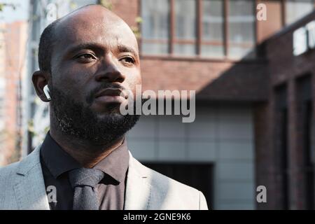 Horizontales Nahaufnahme-Porträt eines selbstbewussten, reifen afroamerikanischen Mannes mit Bart im Gesicht und Ohrstöpseln, der im Freien unterwegs ist und Musik hört, die wie ein aussieht Stockfoto