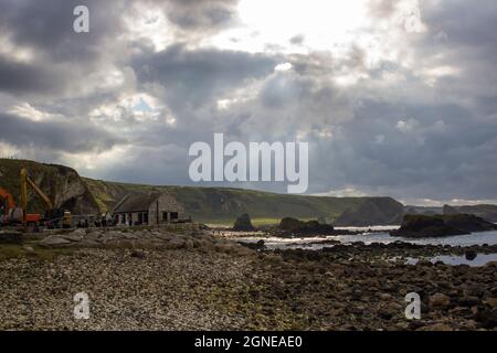 Die Sonne bricht an einem bewölkten Tag im Jahr 2017 durch dunkle Wolken über dem Hafen von Ballintoy in der Grafschaft Antrim in Nordirland Stockfoto