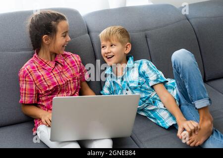 Kleiner Junge mit einem Laptop, der in der Nähe eines Mädchens sitzt Stockfoto