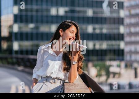 Horizontales Porträt einer attraktiven indischen Frau, die mit ihrem Smartphone eine Sprachnachricht sendet. Sie ist im Finanzdistrikt Stockfoto