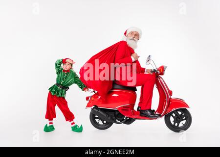 Foto von ernsthaften Menschen Mann Fahrt stecken Moped halten Tasche Kind müde tragen santa Elf Kostüm isoliert grauen Hintergrund Stockfoto