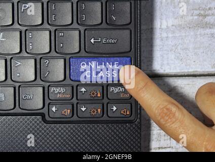 Drücken Sie mit dem Finger auf eine blaue Taste mit der Bezeichnung ONLINE-KLASSE und einem Symbol auf einem Computertastaturkonzept Stockfoto