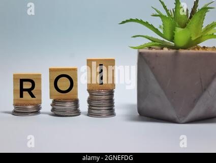 ROI oder Return on Investment Akronym, das auf Holzwürfeln auf nach oben gestapelten Münzen steht. Speicherplatz kopieren. Selektiver Fokus. Unscharfer Hintergrund. Stockfoto