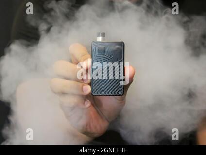 Männliche Hand mit einem E-Zigarette-Vaping-Kit. Selektiver Fokus. Unscharfer Hintergrund. Stockfoto