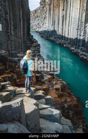 Wanderfrau mit Rucksack genießt den Studlagil Canyon. Einzigartige Jokulsa Basaltkolen und EIN Brufluss. Spektakuläre Outdoor-Szene von Island, Europa Stockfoto