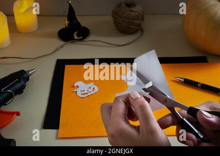 Schritt-für-Schritt-Anleitung. Eine Girlande aus Filz für Halloween. Kürbis und Hexe auf dem Broomstick auf einem Papier ausschneiden. Stockfoto