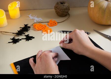 Schritt-für-Schritt-Anleitung. Eine Girlande aus Filz für Halloween. Kürbis und Hexe auf Broomstick mit einer Schere aus Filz ausschneiden. Bereiten Sie Flags A vor Stockfoto