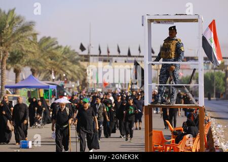 Bagdad, Irak. September 2021. Ein Mitglied der irakischen Sicherheitskräfte (R) beobachtet, wie schiitische Muslime aus Bagdad marschieren, um die Husain-Moschee in Karbala anlässlich von Arba'een, auch bekannt als Chehelom, zu besuchen. Eine religiöse Befolgung, die vierzig Tage nach dem Tag der Aschura stattfindet, um des Martyriums von Husain ibn Ali zu gedenken, dem Enkel des islamischen Propheten Muhammad, der am 10. Tag des Monats Muharram nach islamischem Kalender getötet wurde. Quelle: Ameer Al Mohammedaw/dpa/Alamy Live News Stockfoto