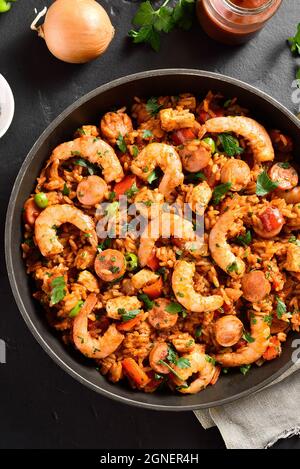 Kreolischer Jambalaya mit Huhn, geräucherten Würstchen und Gemüse in einer Pfanne auf schwarzem Stein. Nahaufnahme Stockfoto