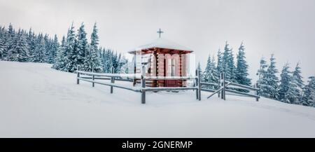 Nebeliges Winterpanorama mit kleiner Kapelle im Bergdorf. Frostige Outdoor-Szene der Karpaten, Bukovel Skigebiet Lage, Ukraine, Europa Stockfoto