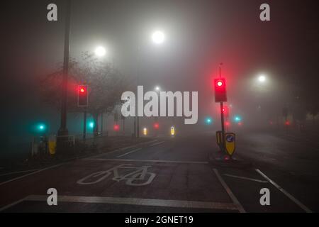 Extrem neblige Nachtbedingungen an einer Kreuzung zweier englischer B-Straßen. Viele Ampeln und Straßenlaternen leuchten durch den atmosphärischen Dunst Stockfoto